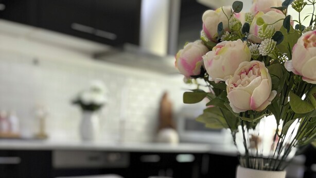 Una mesa de comedor dispuesta con platos blancos, una copa y un jarrón con flores.