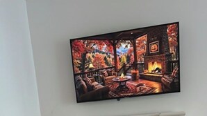 Una sala de estar acogedora con chimenea, un televisor mostrando una escena de hogar y un plato de rollos de canela.