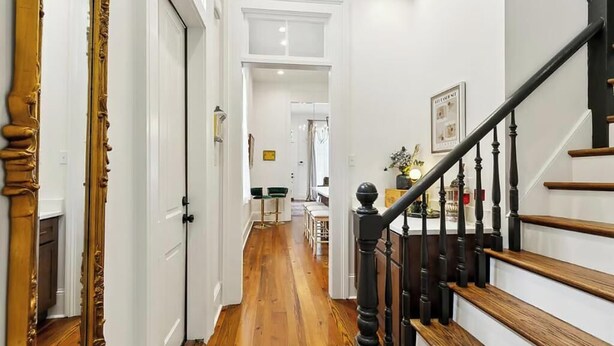 A hallway with wooden flooring, a staircase with black balusters, and white walls. - Hi-End Historic Marigny Gem - Fully Furnished with 2 Bonus Office Space (New Orleans)