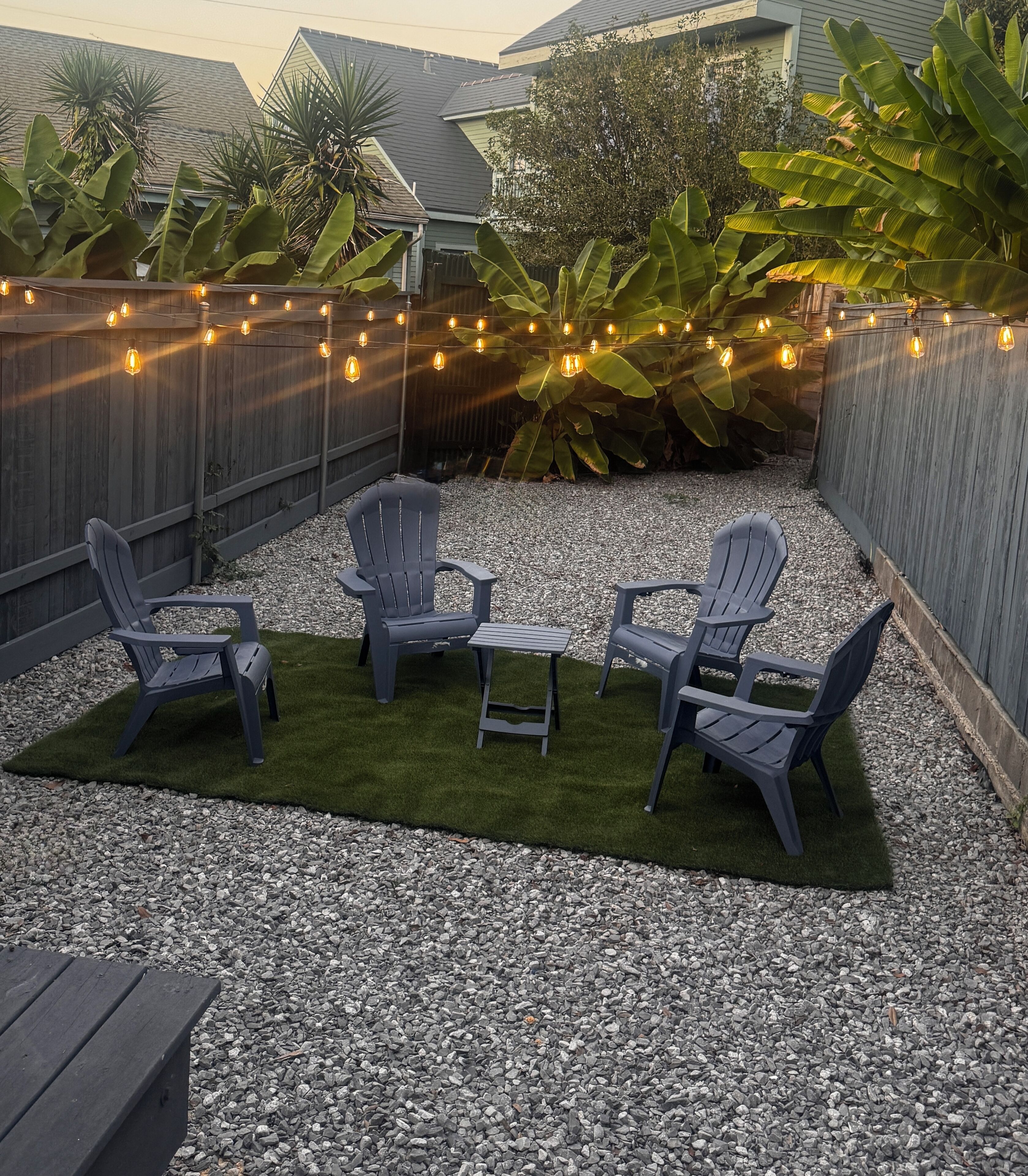 A backyard patio with Adirondack chairs, a small table, and string lights.
