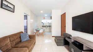 Un salon avec un canapé marron, un pouf gris et un téléviseur à écran plat.