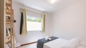 Une chambre à coucher avec un lit, une fenêtre avec des rideaux, une armoire en bois et une petite table.