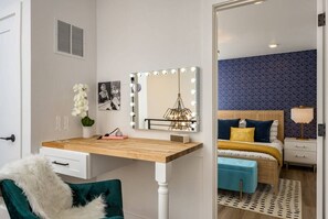 Un dormitorio con tocador, una cama con ropa de cama azul y amarilla, una mesita de noche y un espejo con luces.