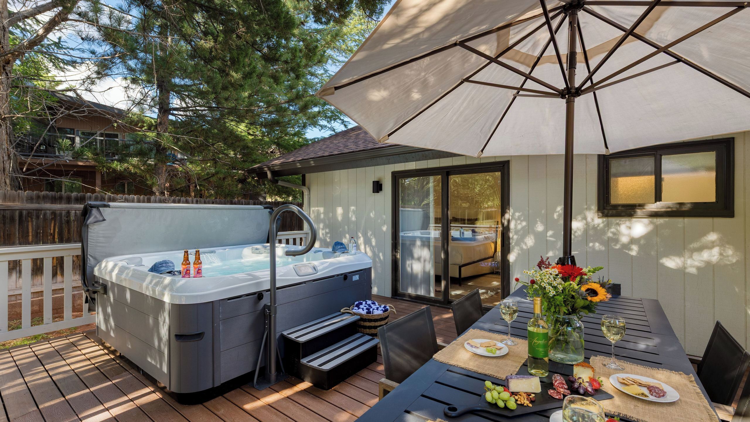 A hot tub on a wooden deck, a table with food and drinks, and a covered patio area.