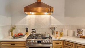 A modern kitchen with a stainless steel stove, a copper range hood, and a tiled backsplash. - Hot Tub, Sauna & Red Rock Views Near Sedona Trails Sedona Serenity Retreat by Avantstay (Sedona)