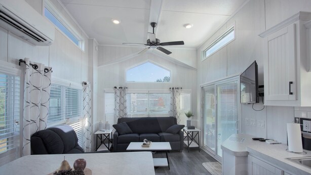A modern kitchen with a dining area, a ceiling fan, and a large window providing natural light. - Tiny Home with AC in charming Hamilton cabin 15 (Hamilton)