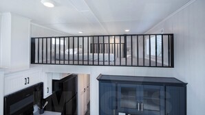 A modern interior with a staircase, a kitchen area, and a dark-colored cabinet. - Tiny Home with AC in charming Hamilton cabin 15 (Hamilton)
