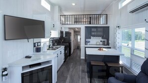 A modern kitchen with white cabinetry, a central island, and a dining area with a bench. - Tiny Home with AC in charming Hamilton cabin 15 (Hamilton)