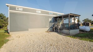 A single-story building with a covered porch and a gravel driveway. - Tiny Home with AC in charming Hamilton cabin 15 (Hamilton)