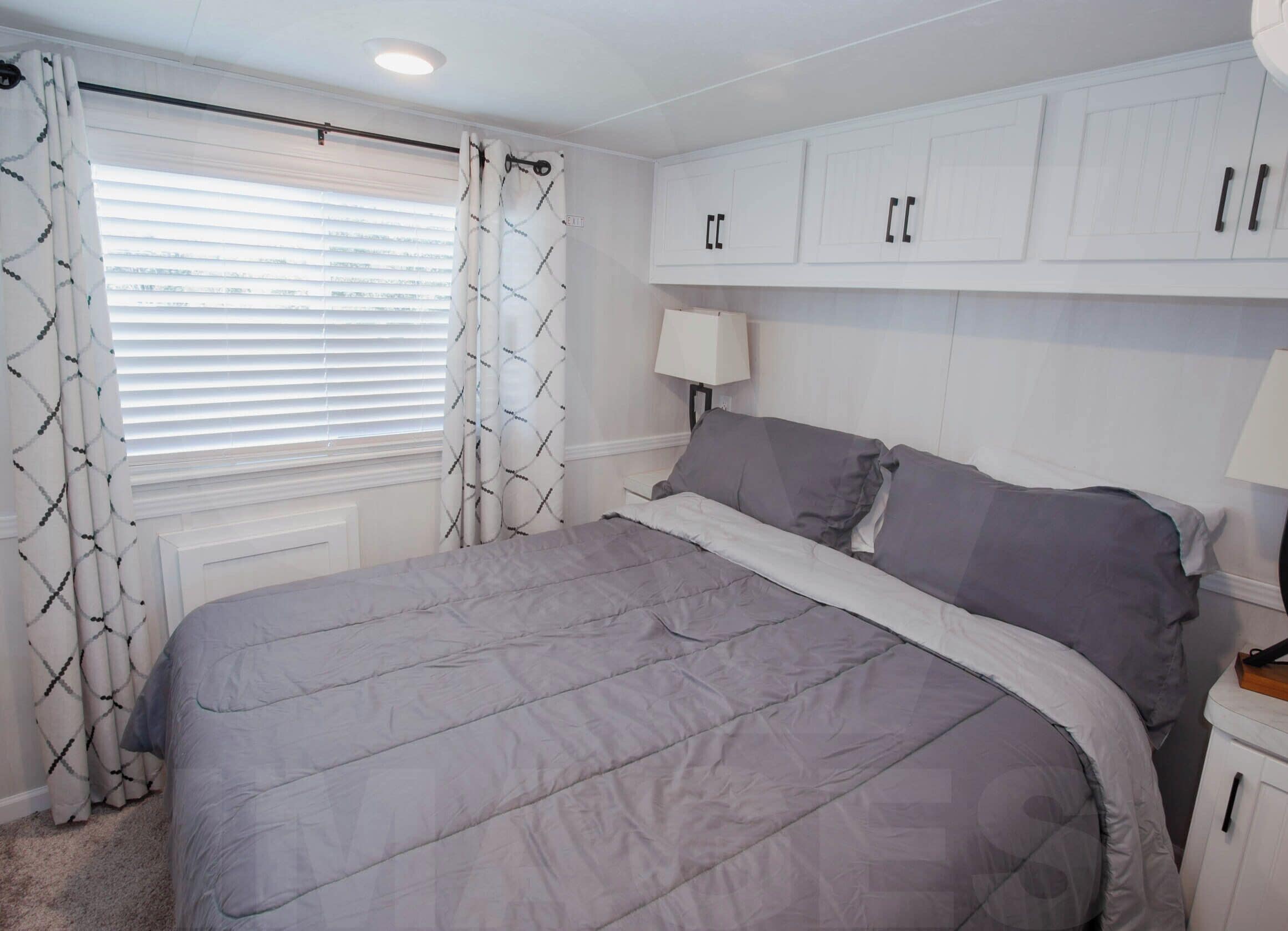 A bedroom with a large bed, white cabinets, and a window with blinds.