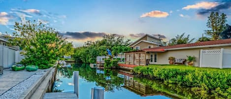 A canal with a wooden dock, houses on one side, and a clear sky.