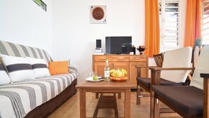 A living room with a sofa, a wooden table with a fruit bowl, a television, and a cabinet. - LEZ'ARLET PLAGE  (Les Anses-d'Arlets)