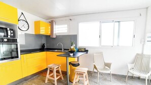 A modern kitchen with yellow cabinets, a black countertop, and a small dining area with two stools and a chair. - LEZ'ARLET PLAGE  (Les Anses-d'Arlets)