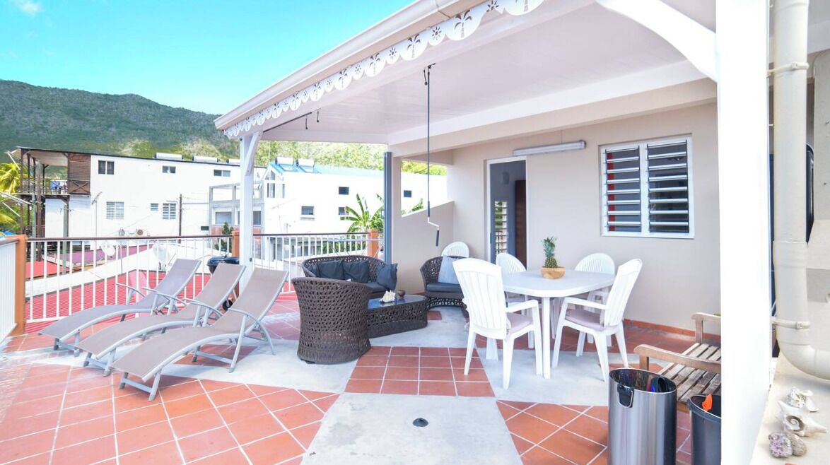 A covered outdoor patio with lounge chairs, a table, and a wicker sofa.
