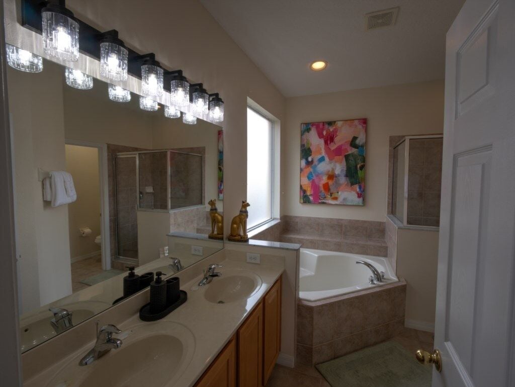 A modern bathroom with a large mirror, two sinks, a bathtub, and a colorful abstract painting on the wall.