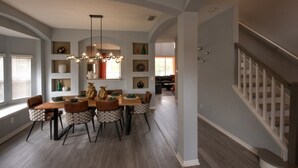A dining area with a wooden table and chairs, a chandelier, and a staircase leading to another level.