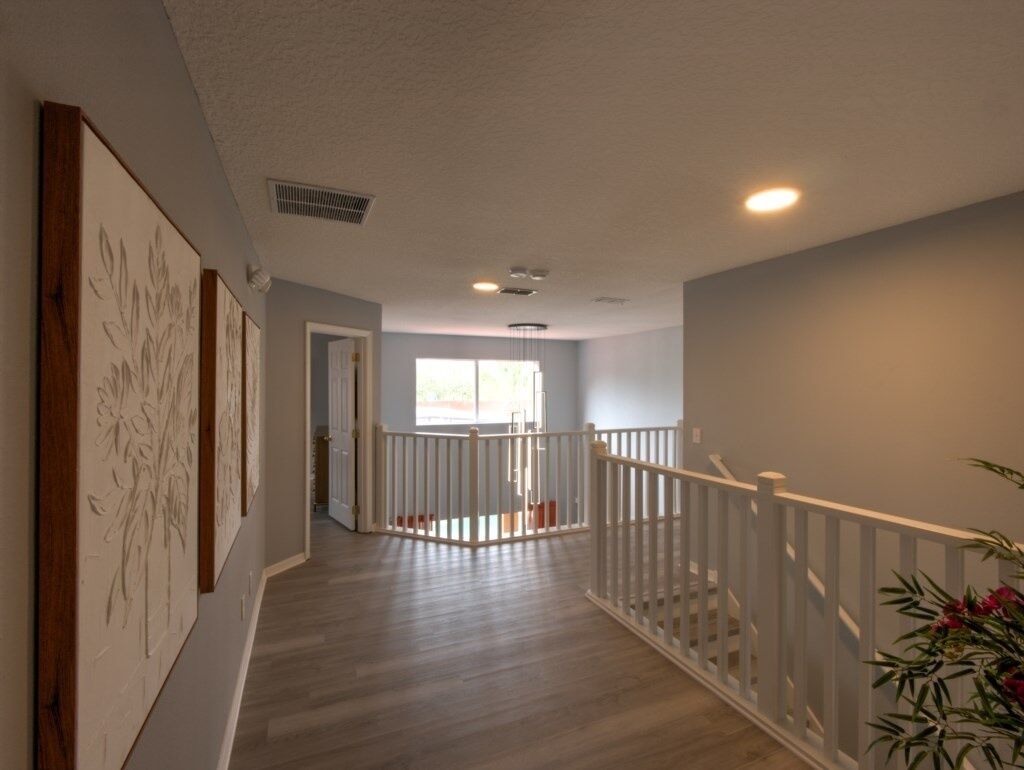 Un pasillo con suelo de madera, barandillas blancas y una puerta que da a otra habitación.