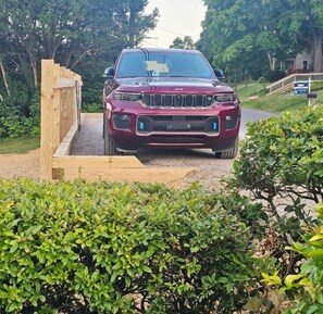 A maroon SUV parked on a gravel path with a wooden fence and greenery in the background. - Dean Lake House (Watkins Glen)