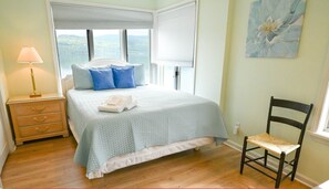 Ein Schlafzimmer mit Bett, Nachttisch, Stuhl und Fenster mit Blick ins Freie.