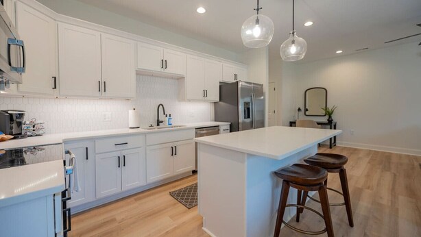 A modern kitchen with white cabinets, a stainless steel refrigerator, and a central island with stools. - Brand-New 3BR Townhome | KING BED | Great Location (Lynchburg)