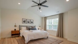 A bedroom with a bed, a nightstand, a ceiling fan, a window with curtains, and framed pictures on the wall. - Brand-New 3BR Townhome | KING BED | Great Location (Lynchburg)