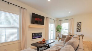 A modern living room with a large flat-screen TV, a fireplace, and a comfortable sofa. - Brand-New 3BR Townhome | KING BED | Great Location (Lynchburg)