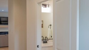 A hallway with a wooden floor leading to a bathroom with a sink and mirror. - Brand-New 3BR Townhome | KING BED | Great Location (Lynchburg)