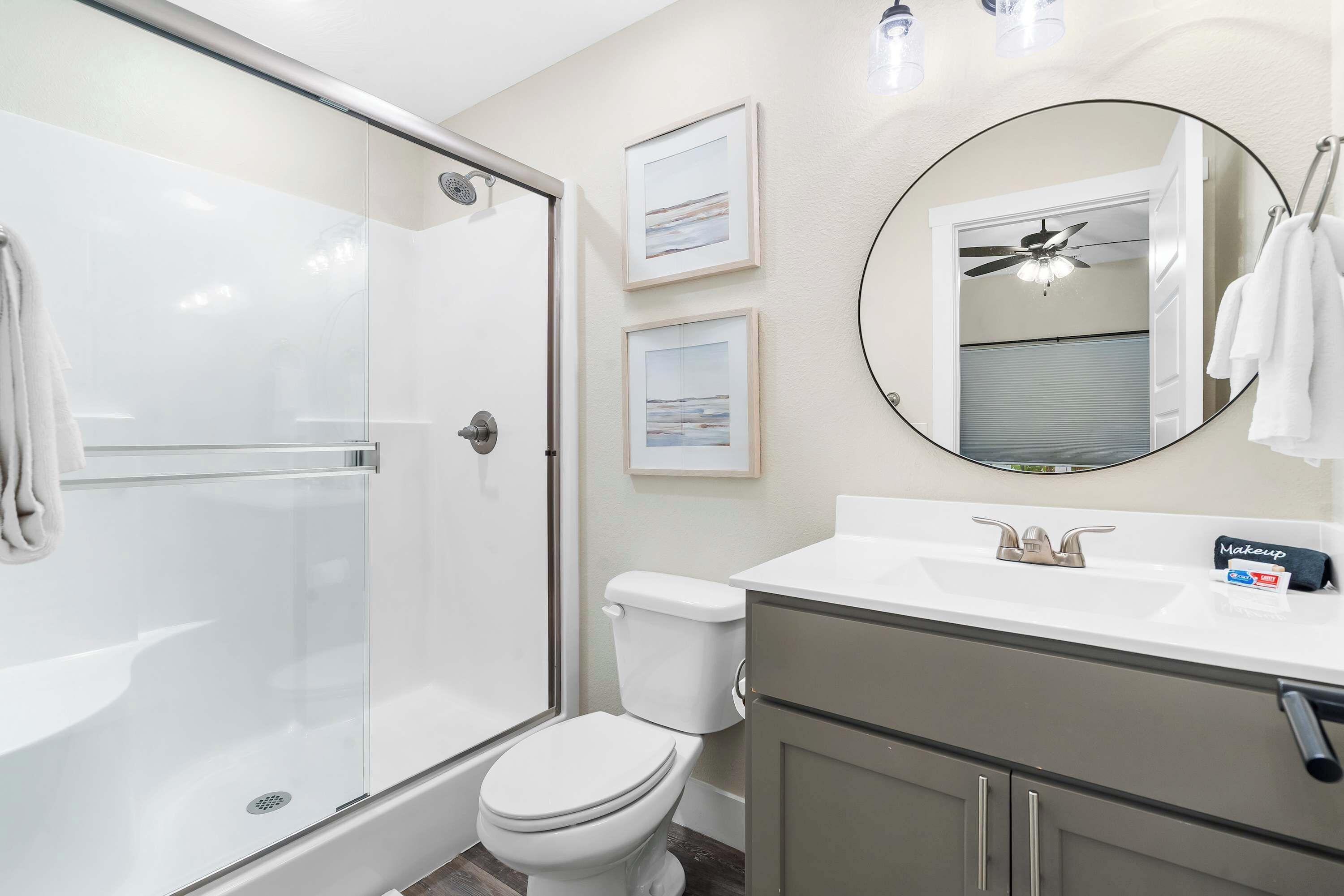 A bathroom with a glass shower enclosure, a toilet, a sink with a vanity, and a mirror.