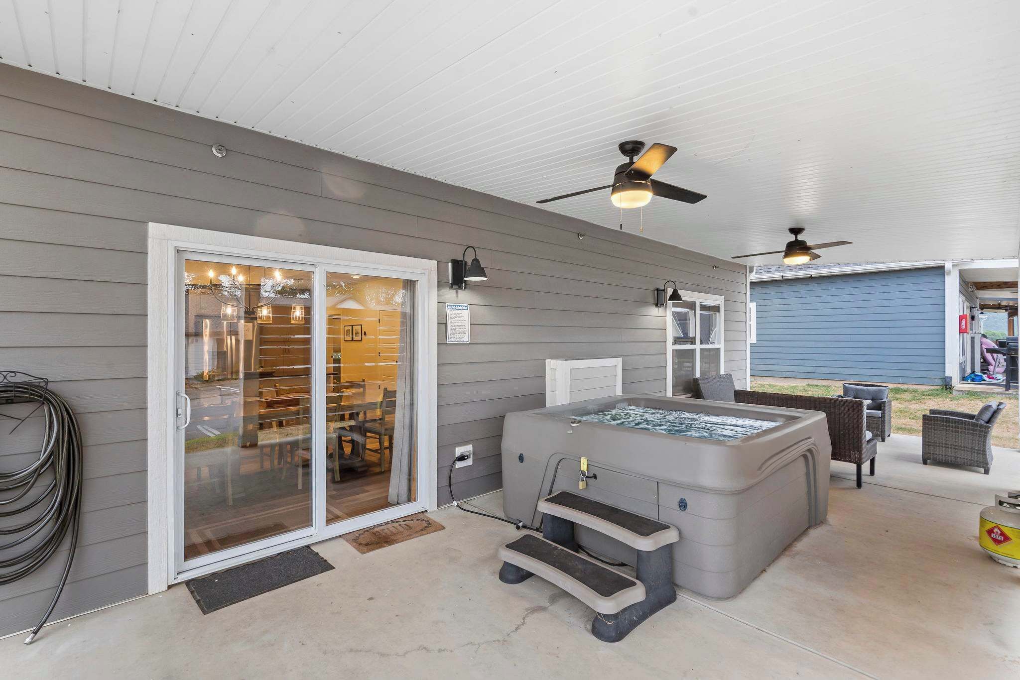 An outdoor patio with a hot tub, ceiling fans, and outdoor seating.