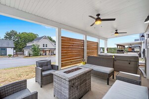 An outdoor patio area with wicker furniture, a fire pit, ceiling fans, and a view of neighboring houses.