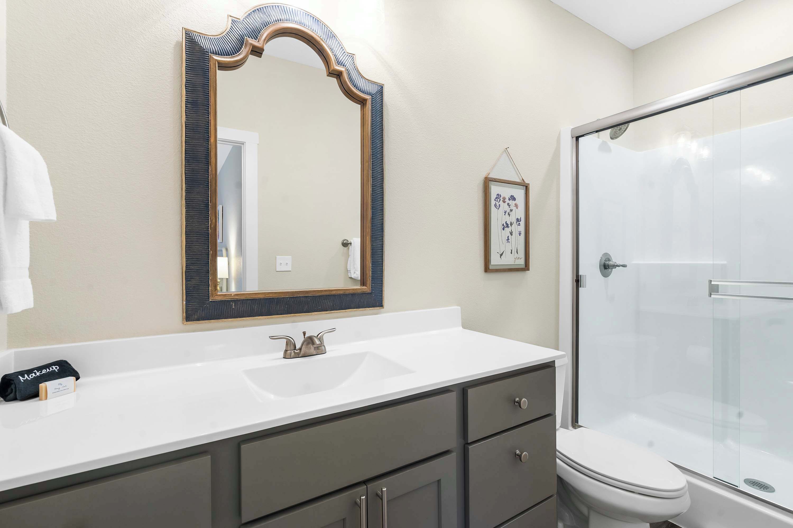 A bathroom with a white sink, a large mirror, a framed picture on the wall, and a glass-enclosed shower.