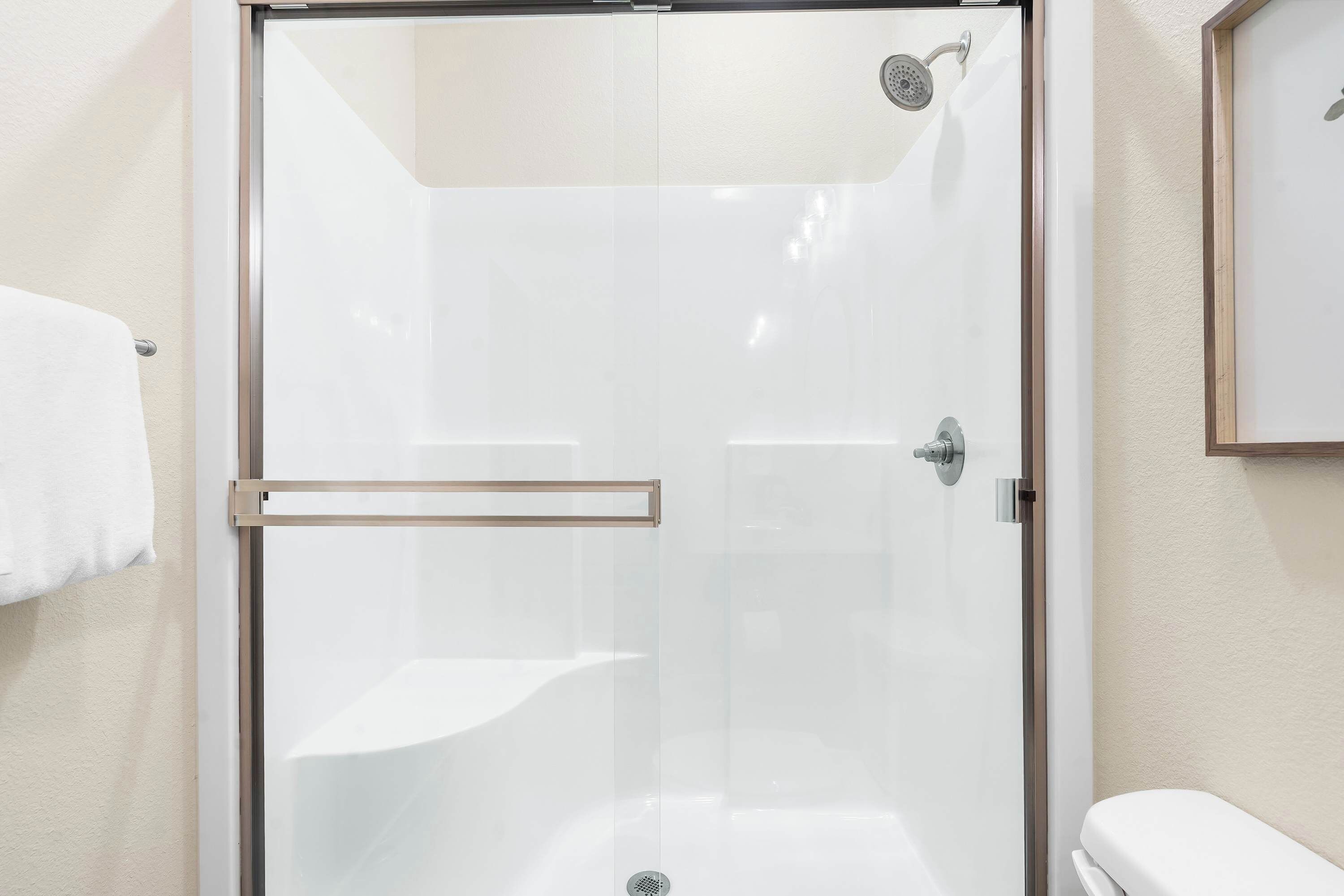 A glass-enclosed shower with a metal handle and a showerhead.