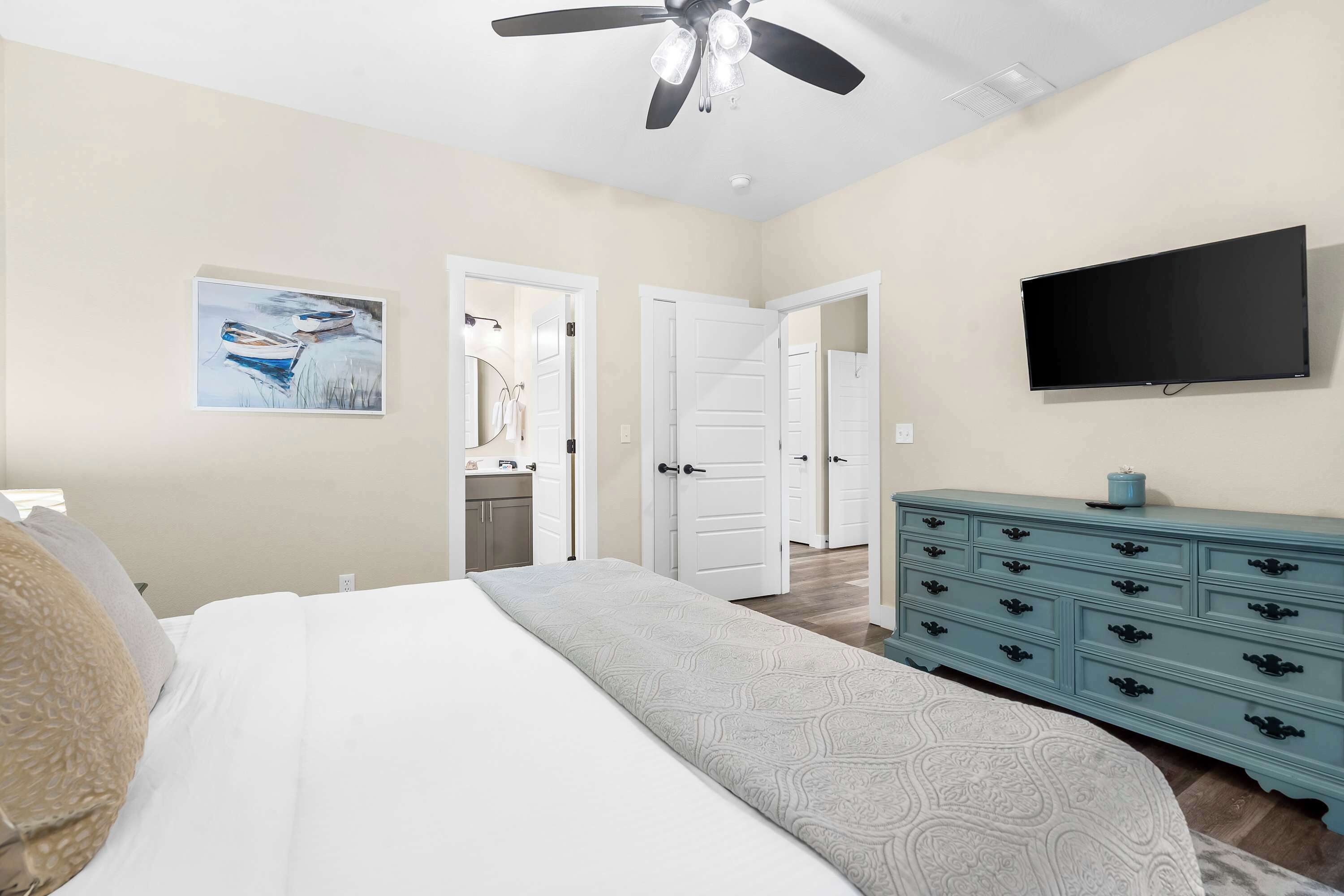Een slaapkamer met een bed, een plafondventilator, een televisie, een dressoir en een deur naar een andere kamer.