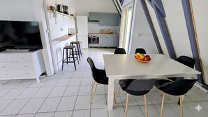 Une cuisine moderne avec un coin repas, des meubles blancs et un téléviseur.