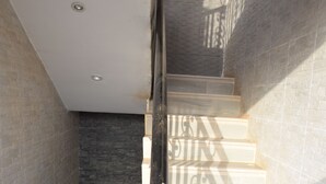 A staircase with a metal handrail, leading to a landing with a dark wall and a light-colored floor. - Terra Santa Lodgings & Restaurants (Adentan)