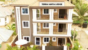A multi-story building named Terra Santa Lodge with a central balcony, a gated entrance, and two parked vehicles in front. - Terra Santa Lodgings & Restaurants (Adentan)