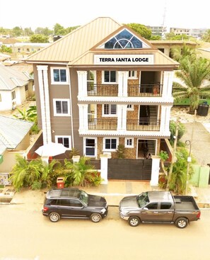 A multi-story building named Terra Santa Lodge with a central balcony, a gated entrance, and two parked vehicles in front. - Terra Santa Lodgings & Restaurants (Adentan)