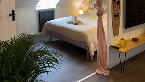 Ein gemütliches Schlafzimmer mit schrägen Wänden, einem Himmelsbett, einem an der Wand befestigten Surfbrett und einem Fernseher.