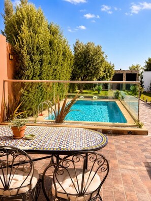 A pool with a tiled deck, surrounded by trees and a clear sky.