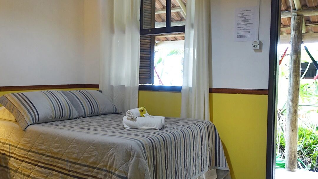 Una cama individual con una colcha a rayas, una toalla enrollada y una ventana con cortinas.