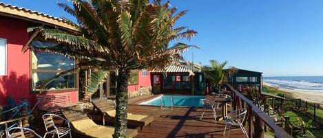 A wooden deck with lounge chairs, a swimming pool, and a view of the ocean.