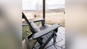 A covered outdoor seating area with a single black lounge chair and a patterned pillow.