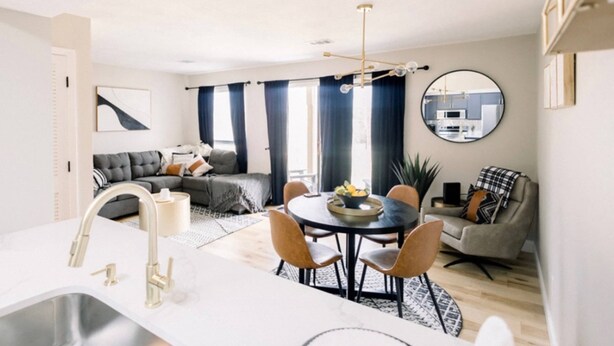 A modern living room with a dining area, a kitchen, and a large window with curtains.