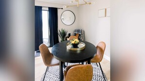 A dining area with a round table, four chairs, a modern chandelier, and a potted plant.