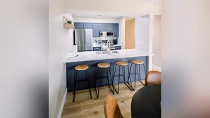 A modern kitchen with a white countertop, stainless steel appliances, and wooden bar stools.