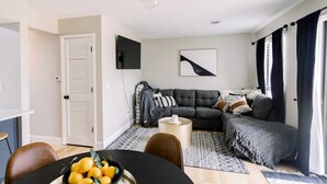 A modern living room with a sectional sofa, a flat-screen TV, and a dining area with a table and chairs.