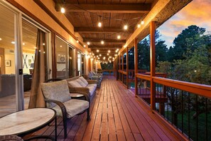 Un terrazzo in legno con posti a sedere all'aperto, luci decorative e vista sugli alberi.