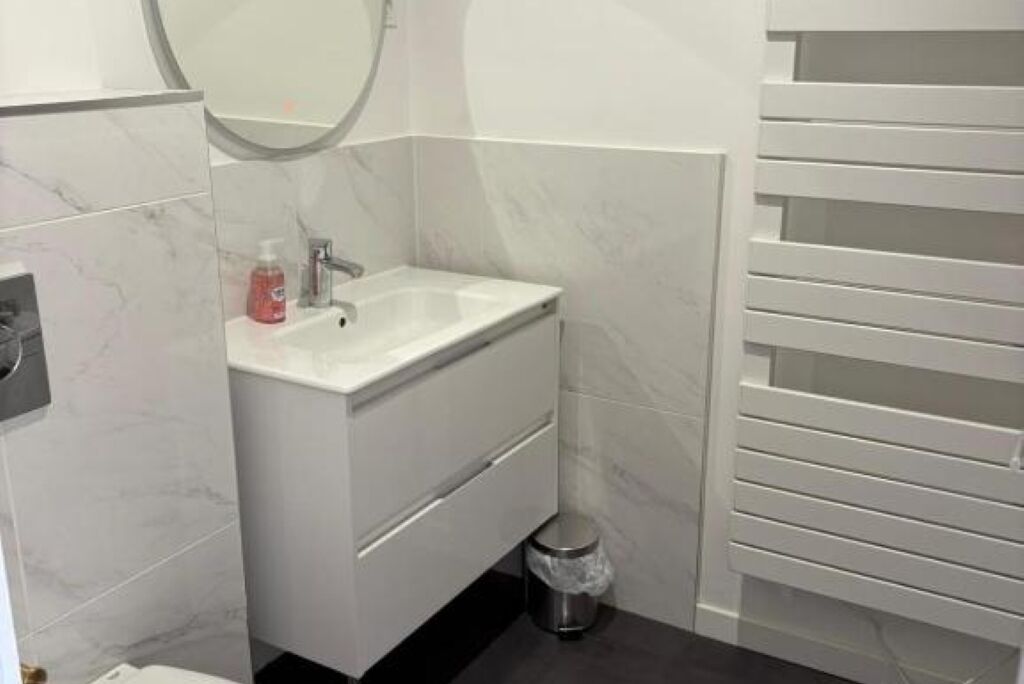Un baño con un lavabo blanco, un espejo y un cubo de basura.
