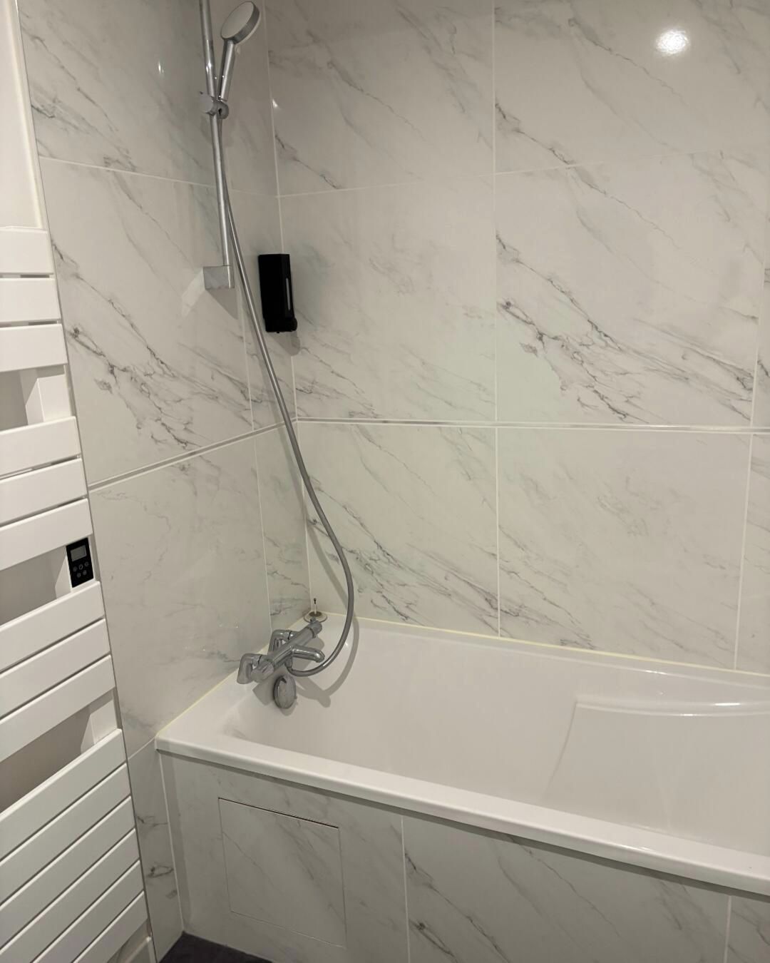 Un bany modern amb una dutxa d'encoixinat de marbre blanc, un panell de control i una banyera.