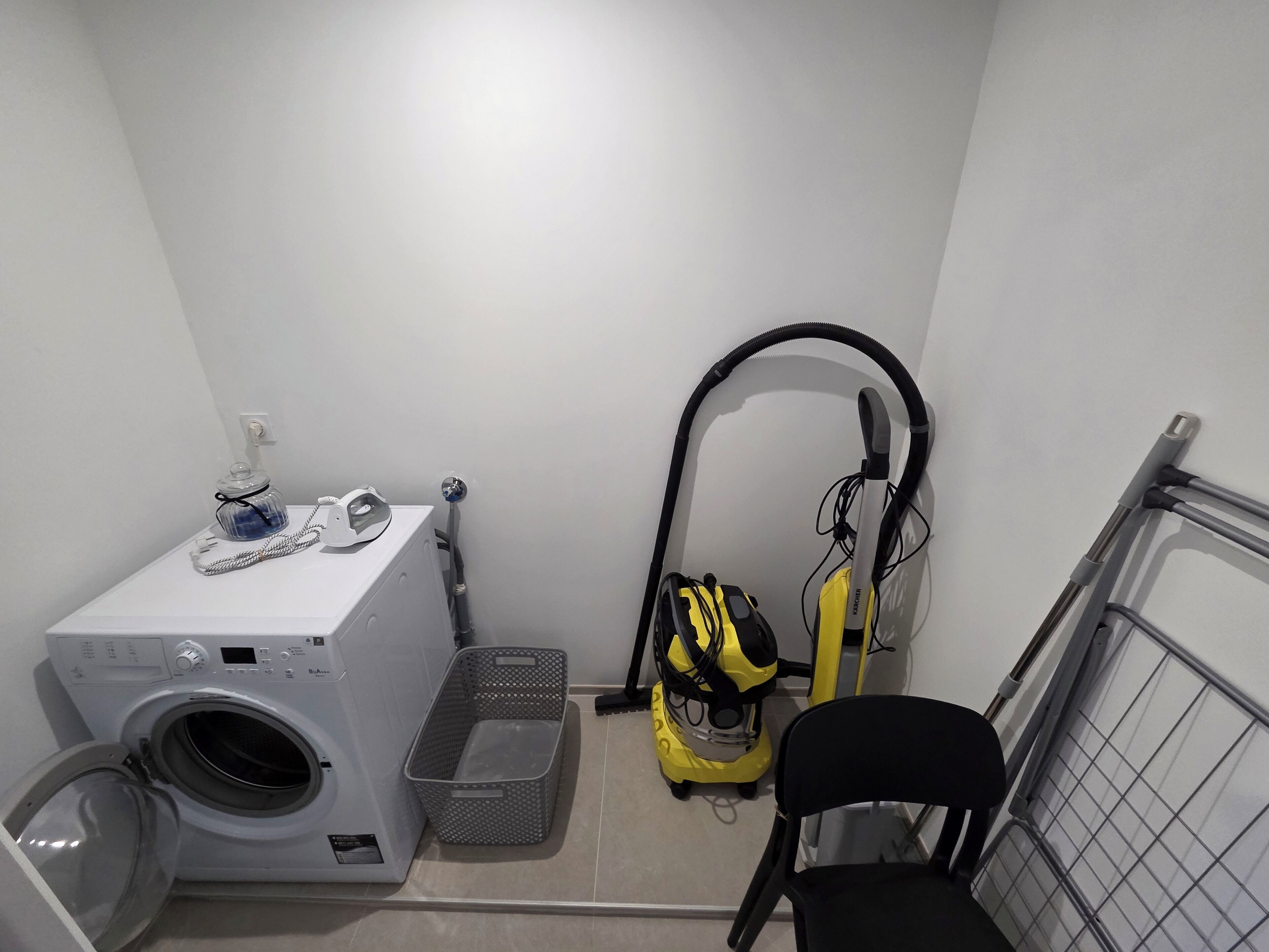 A laundry room with a washing machine, a dryer, a vacuum cleaner, and a chair.